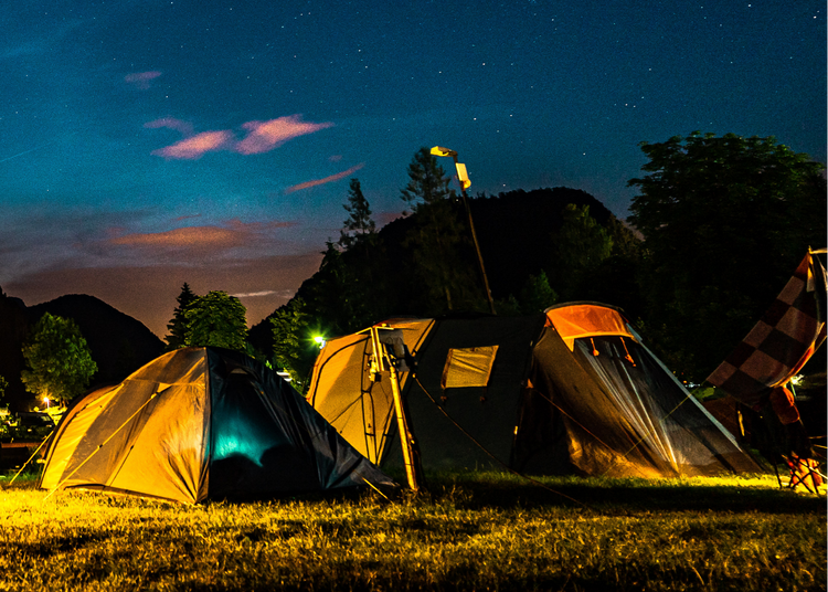 Camping scene with tents illuminated at night against a mountainous background