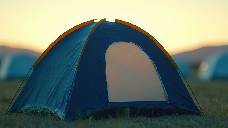 Blue camping tent in a field with a sunset or sunrise in the background