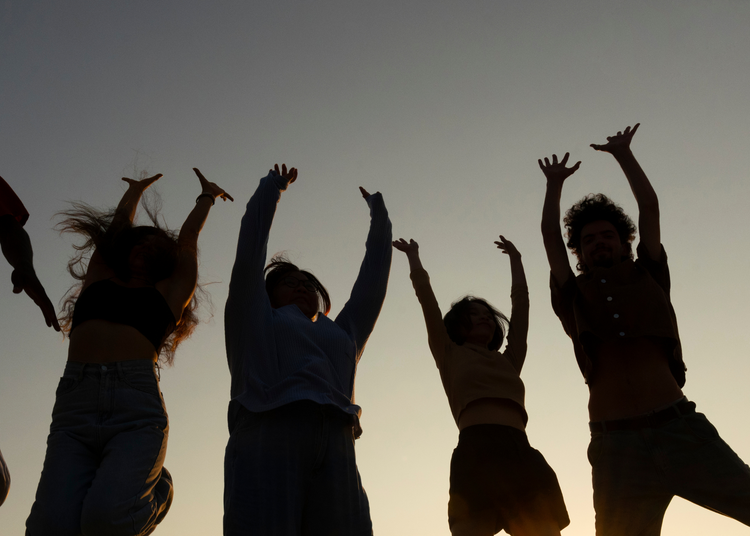 Silhouettes of people jumping against a sunset sky